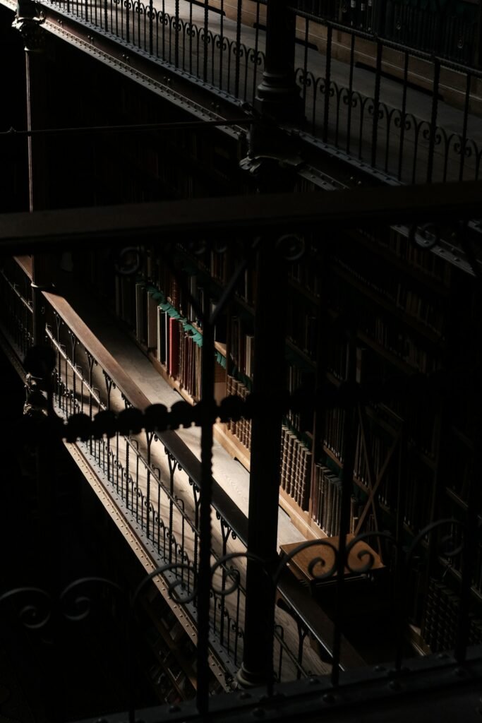 Sunlight reaching bookshelves beneath decorative railings in a dark library